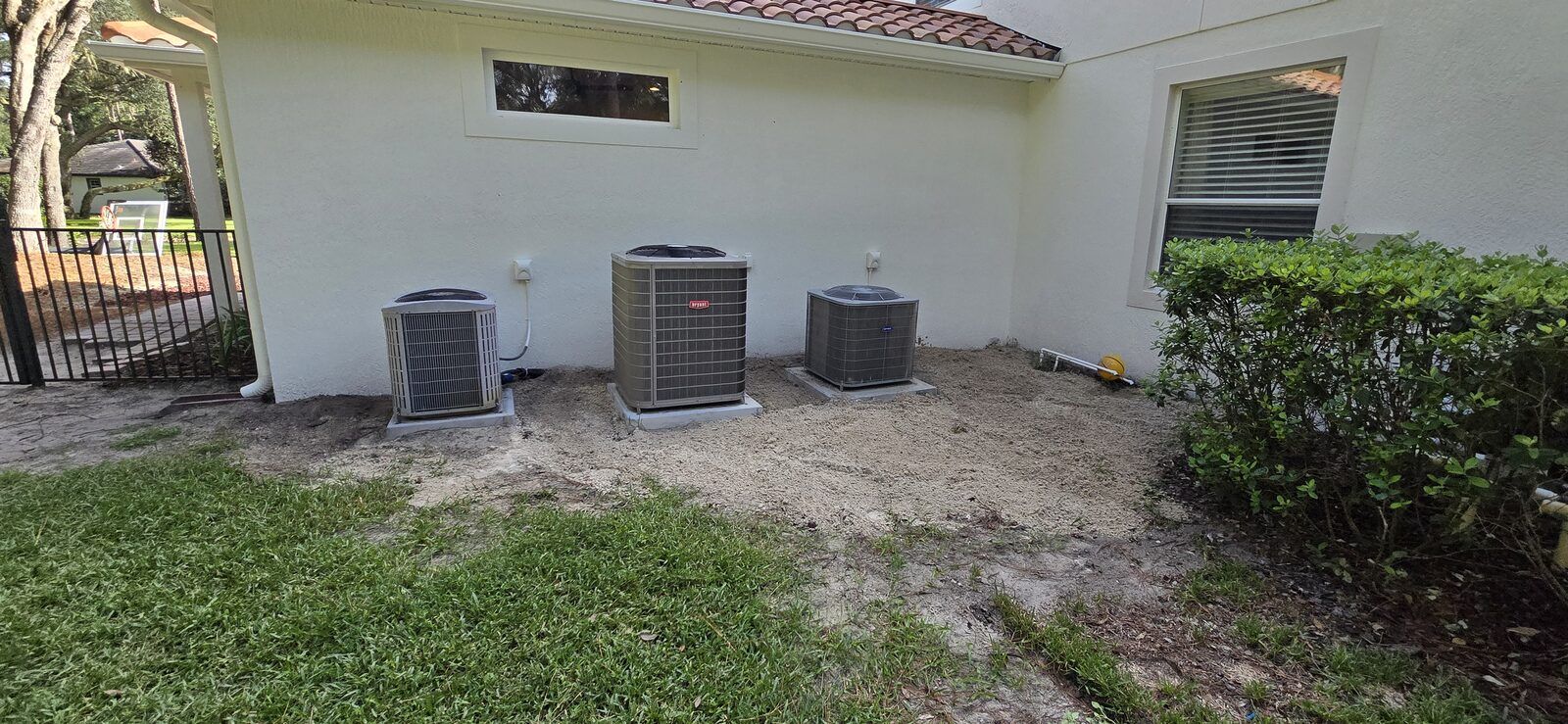 Backyard with three AC condenser units on fresh pads and a basketball hoop standing in the background
