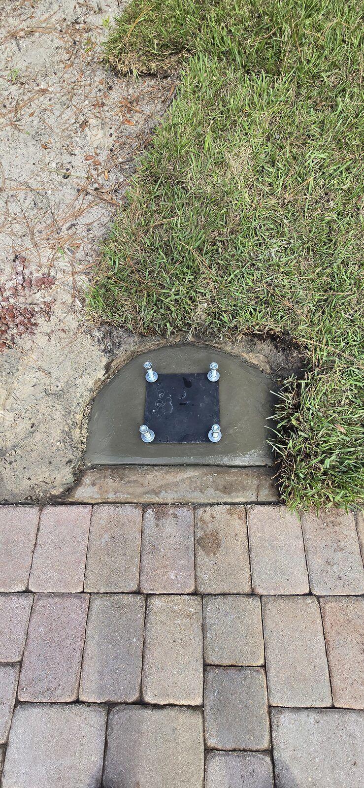 Basketball hoop anchor plate with four J-bolts set dead level in fresh concrete beside pavers