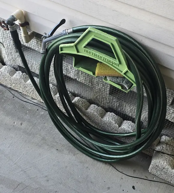Green garden hose coiled by an outdoor spigot, ready to fill a portable basketball hoop base with water