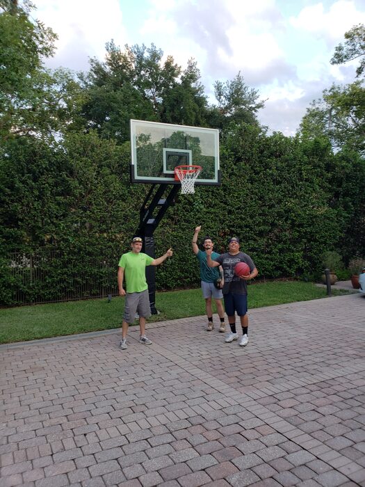 Three guys celebrating under a freshly installed in-ground basketball hoop on a paver driveway