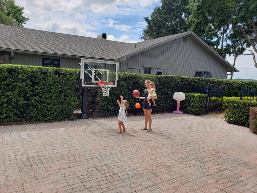 Mom and two kids shooting hoops on a backyard paver court