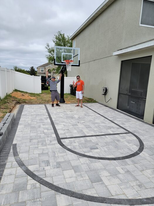 Two customers standing on a new paver basketball court with painted key lines