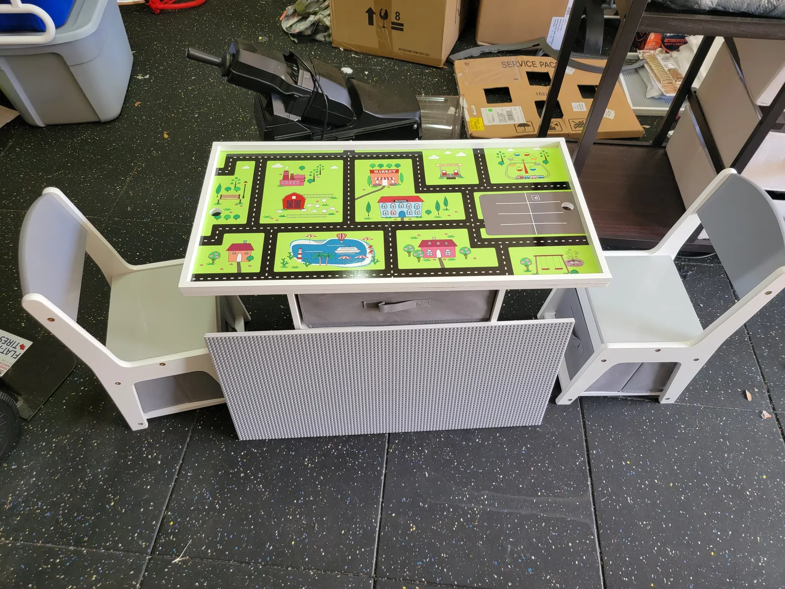 Kids activity play table with road map top, storage bin and two chairs assembled in a Florida garage