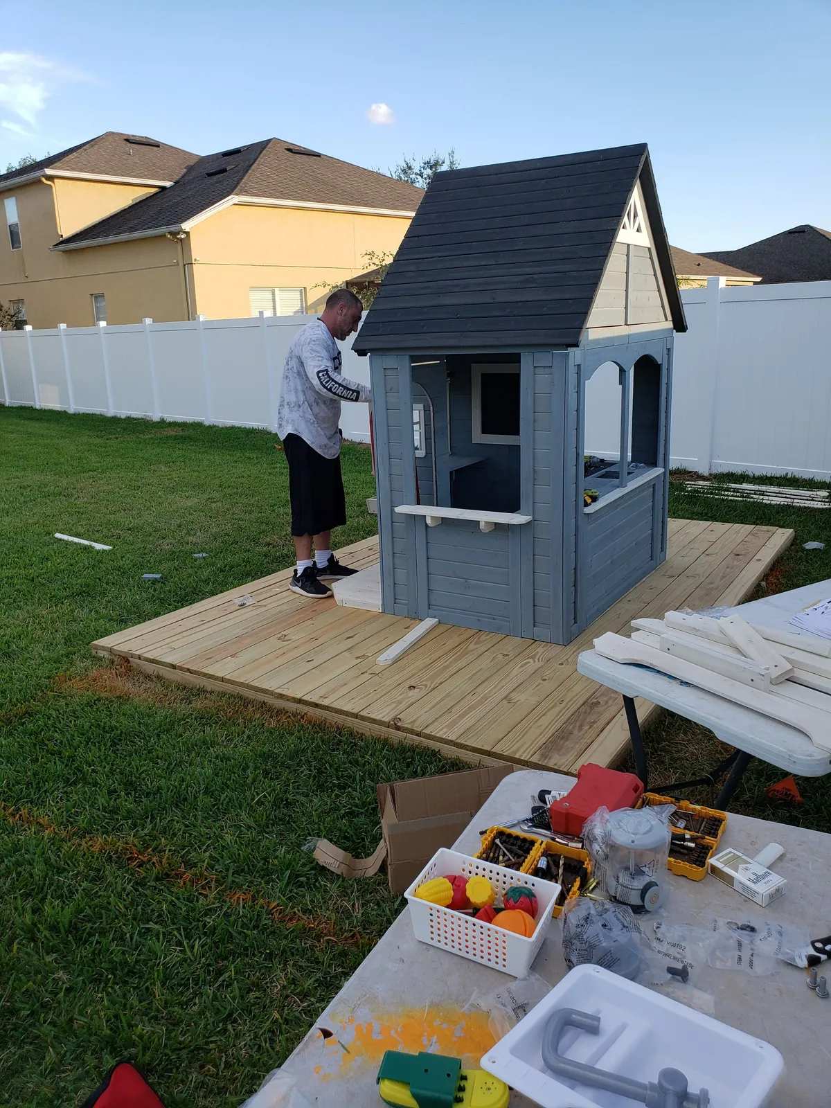 DR Assembly technician assembling a wooden childrens playhouse on a backyard deck in Florida