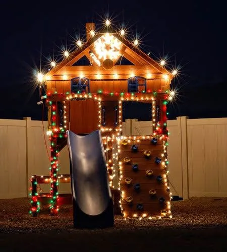 Wooden playset and playhouse fully assembled and lit up with Christmas lights at night in a Florida backyard