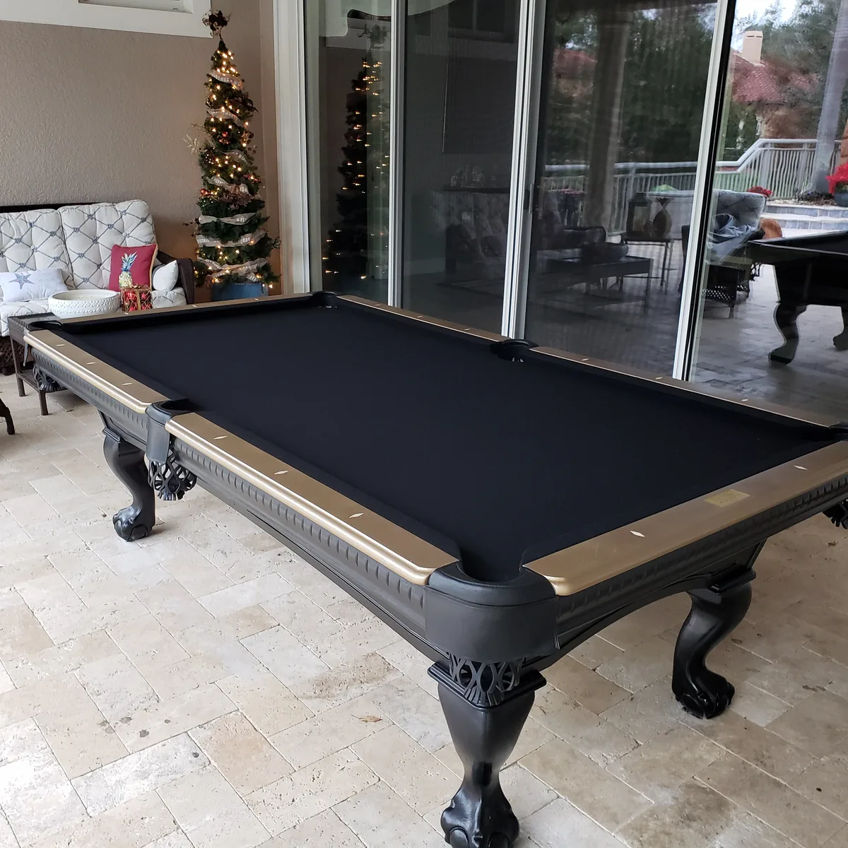 Black and gold slate pool table professionally assembled on a travertine lanai beside a lit Christmas tree in Largo, Florida, felt brushed and rails installed by DR Assembly