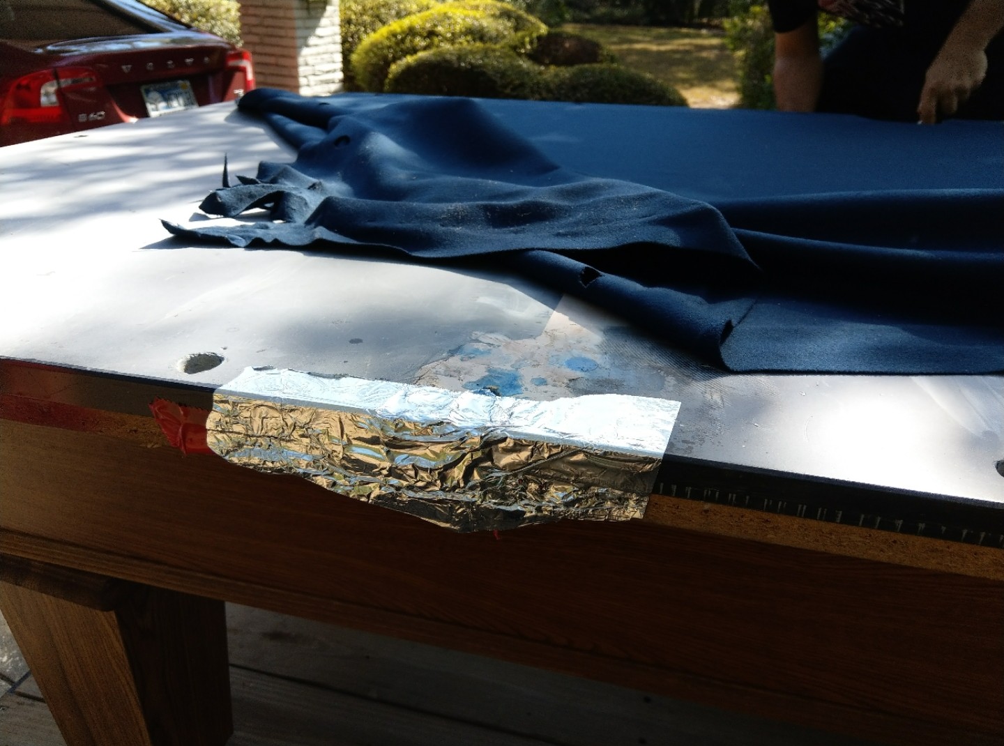 Pool table slate with cloth pulled back revealing a taped seam repair — this is why residential tables use three-piece slate