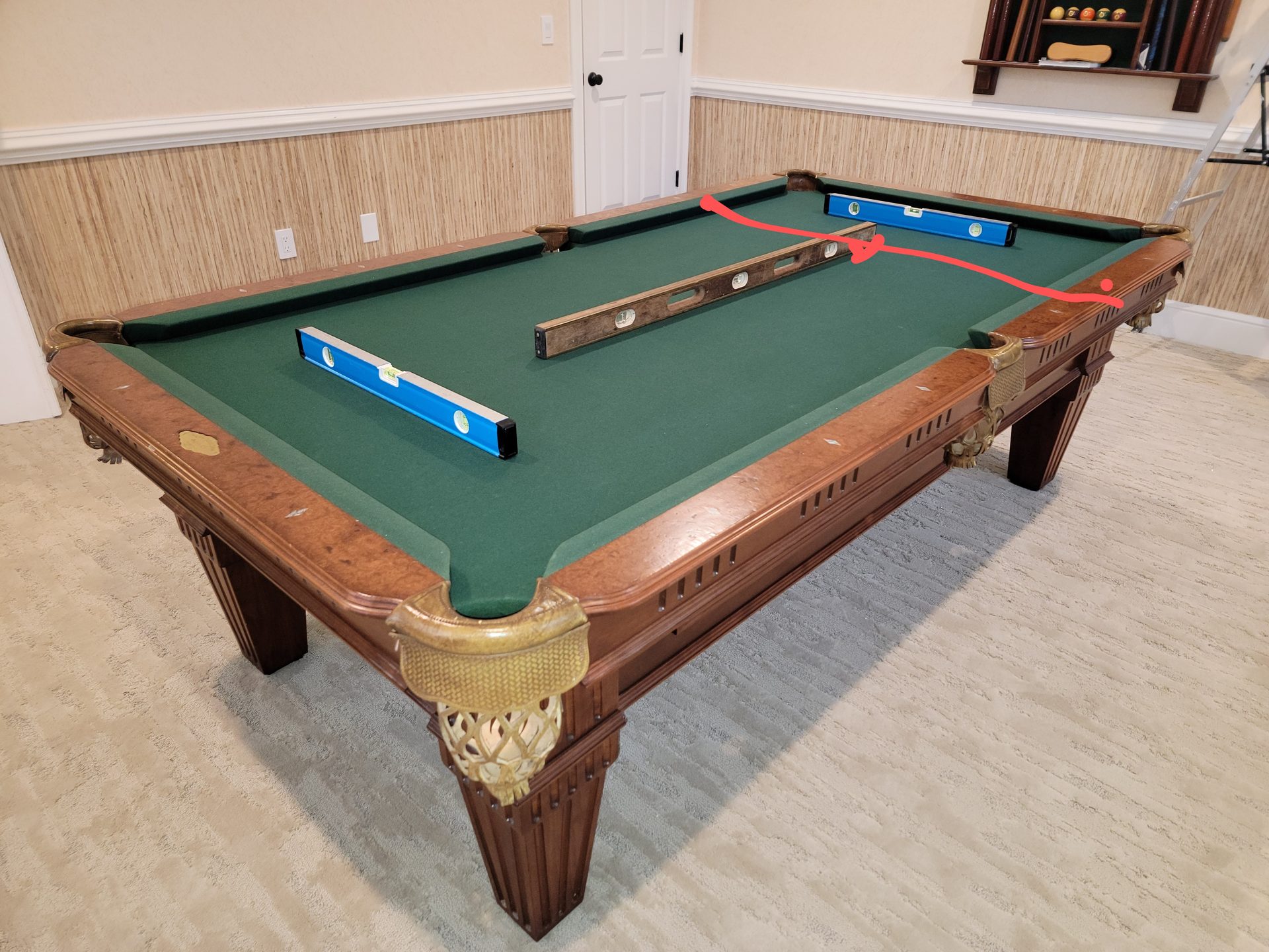 Ornate wood pool table with blue machinist levels checking dead-level across the green felt — Brunswick Olhausen specialty