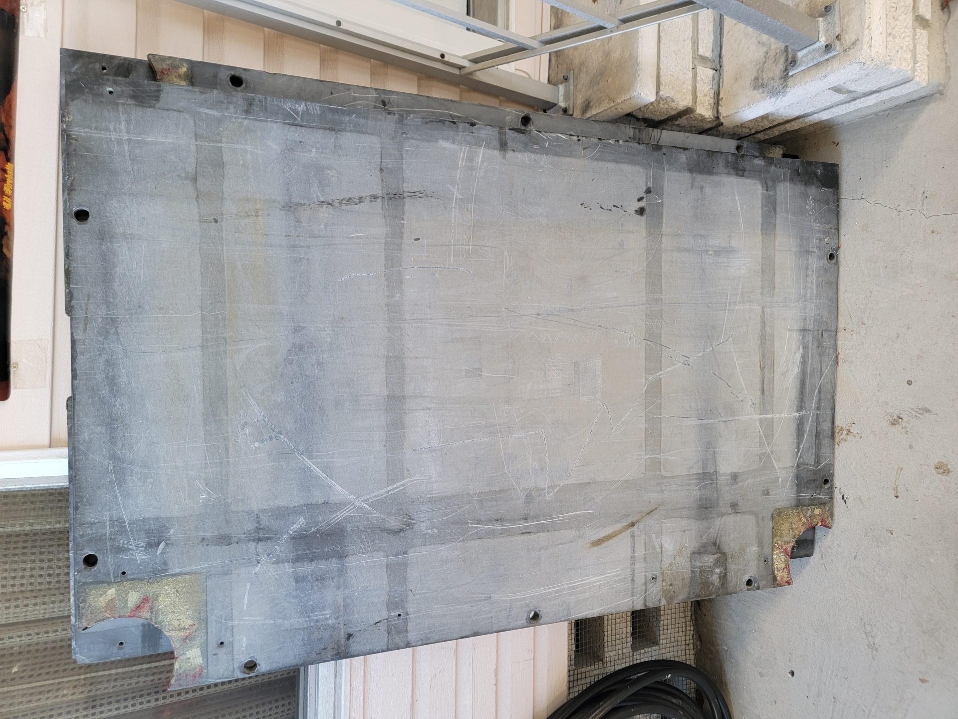 Raw three-piece pool table slate slab leaning against a wall showing drill holes and weight