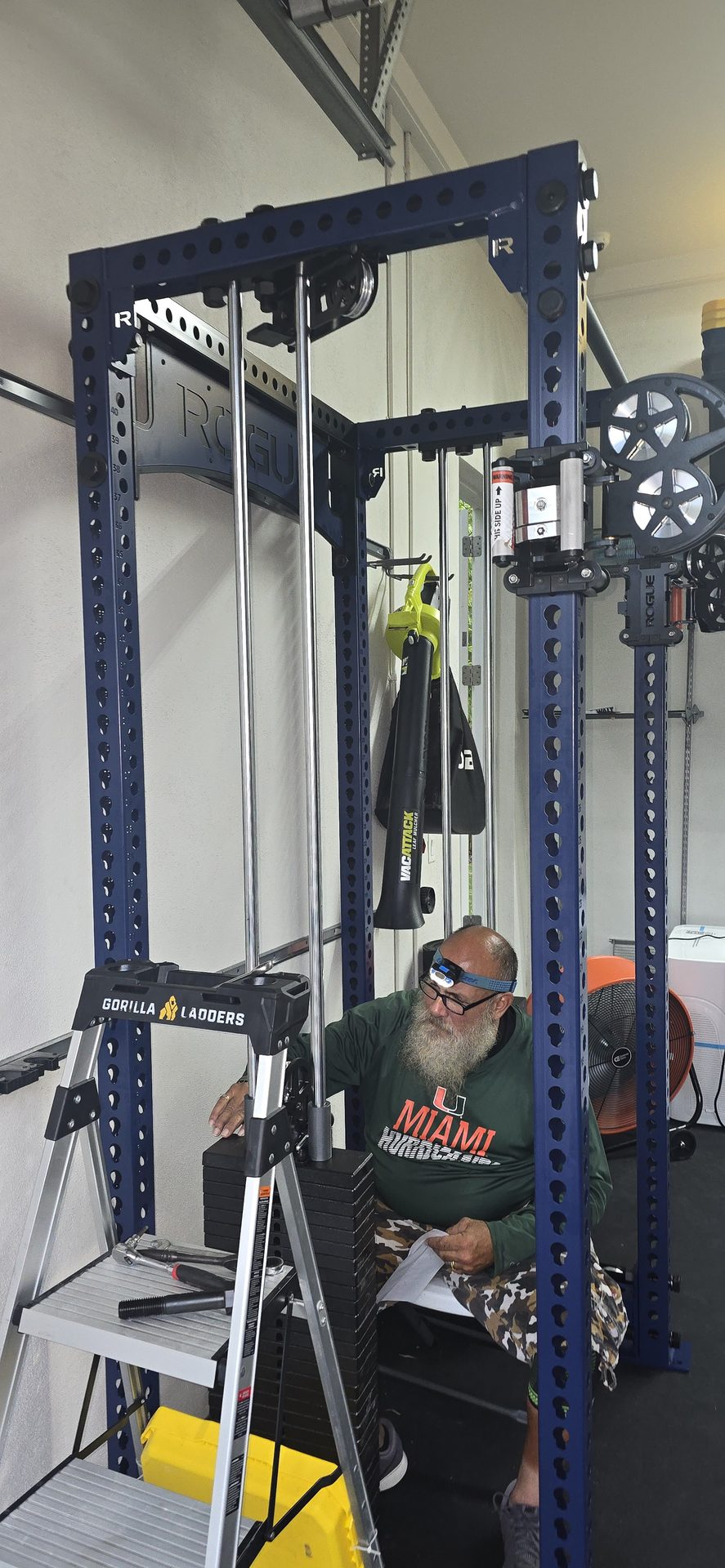 DR Assembly technician reviewing manual while assembling Rogue FM-3 Indy Functional Trainer with Gorilla ladder and tools