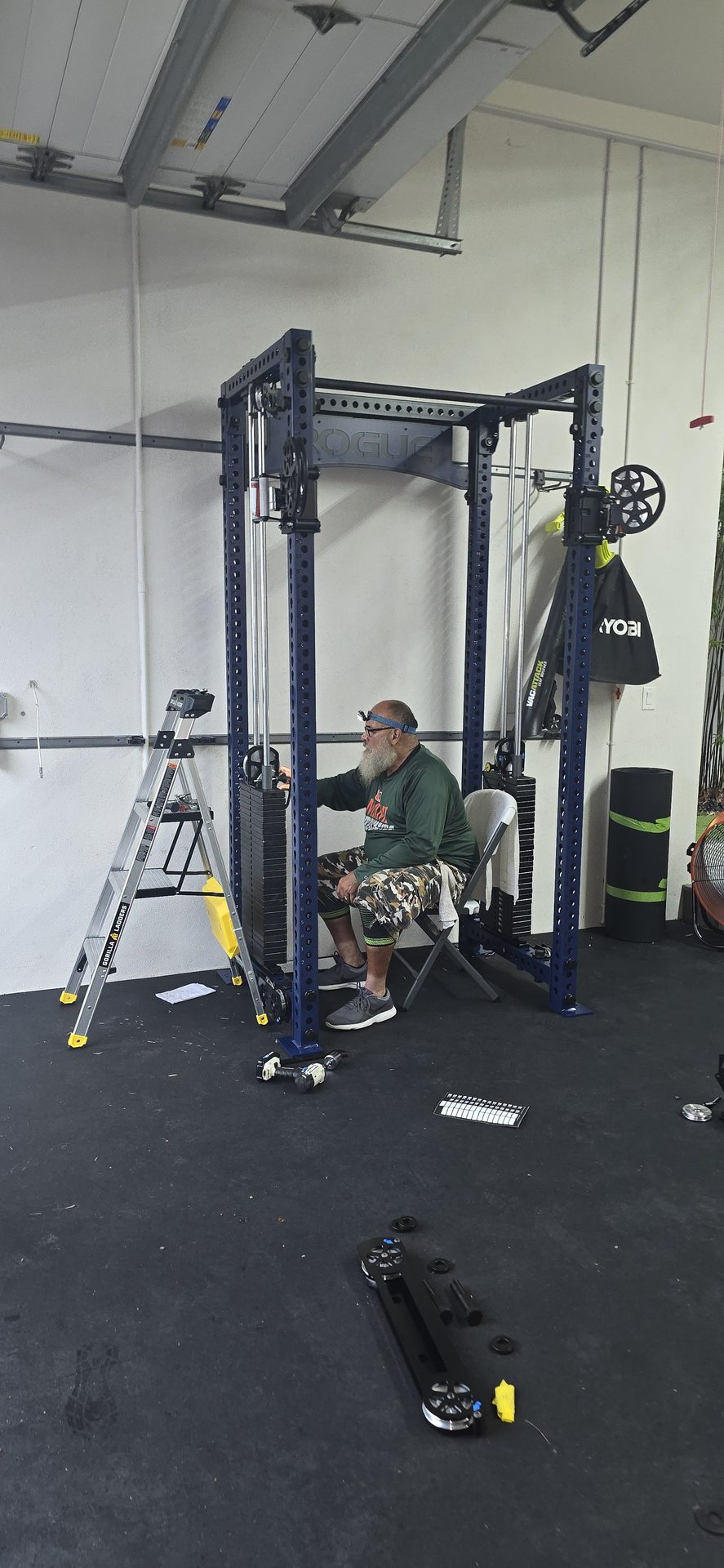 DR Assembly technician seated inside Rogue FM-3 Indy Functional Trainer frame during assembly with weight stacks and pulley system visible